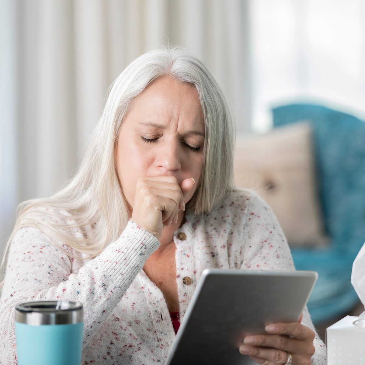 Senior woman coughs while having telehealth appointment on digital tablet with her doctor