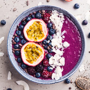 Tasty appetizing smoothie acai bowl made from blackberries and wild berries, decorated with cut passion fruit, coconut flakes, and cacao nibs. Served in bowl. Healthy life clean eating concept.