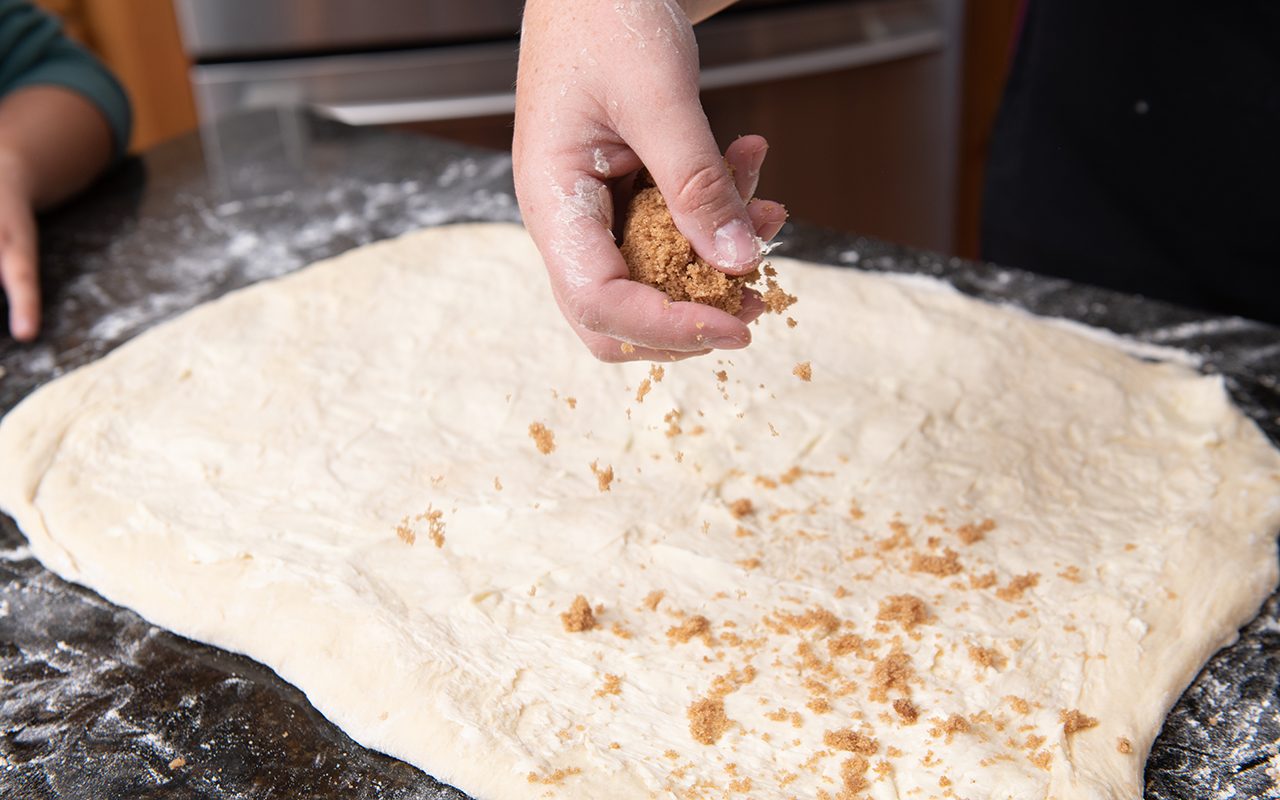 Cristen Clark sprinkling brown sugar on cinnamon roll dough