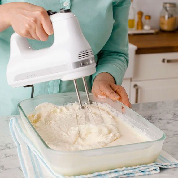 person using a hand mixture that has thickened on mixture in a glass 13x9 pan