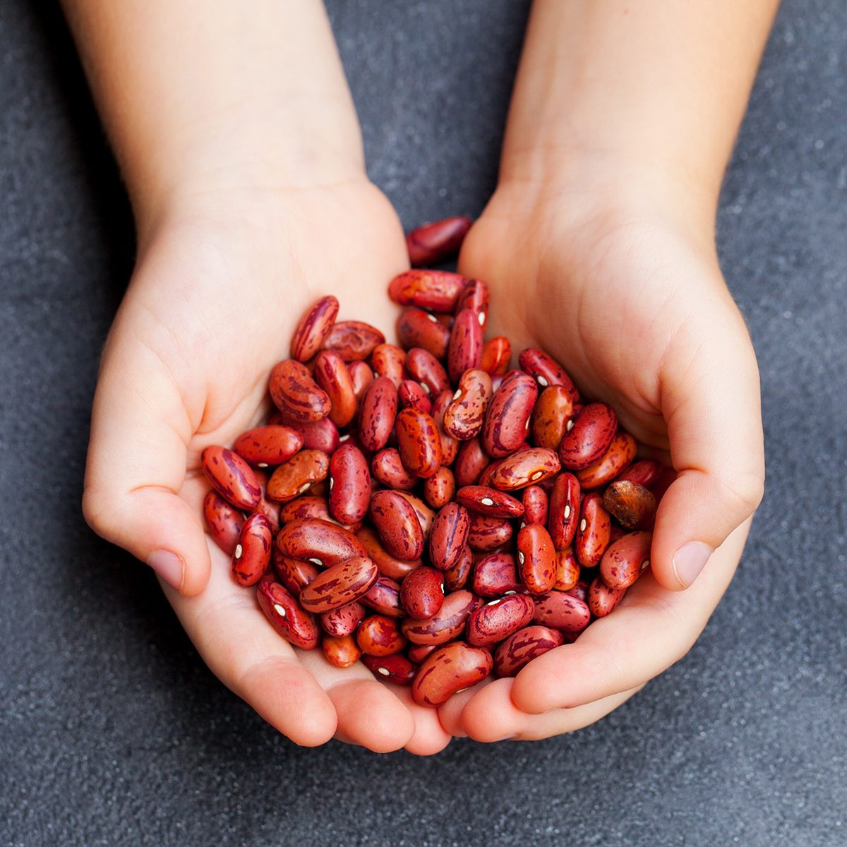 Red kidney beans in kids hands. Grey stone background. Top view