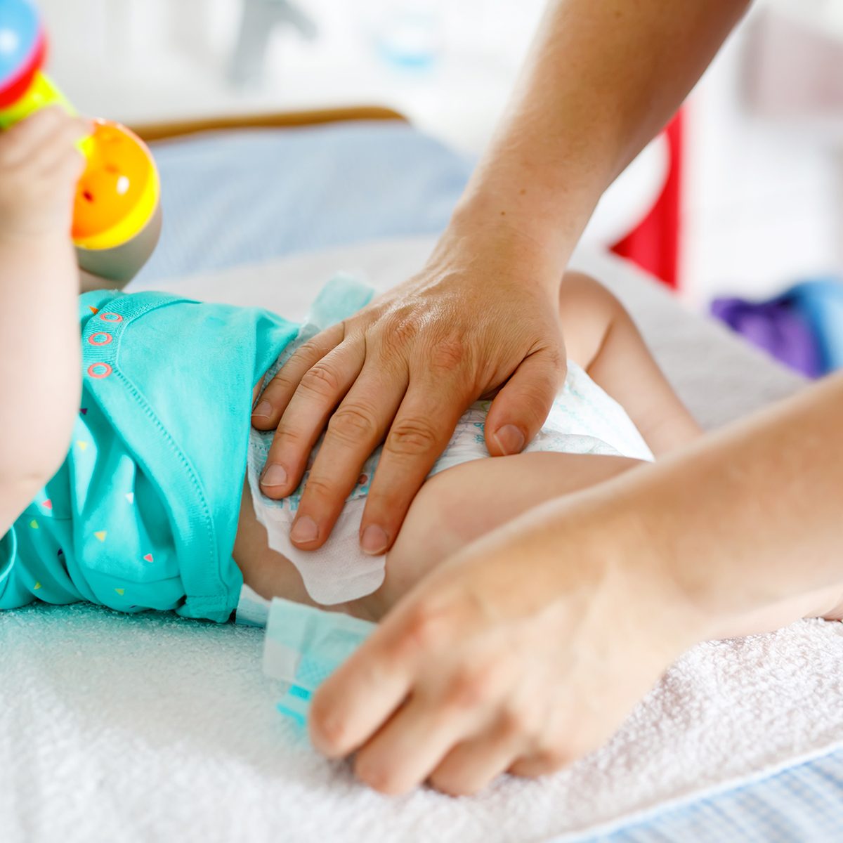 Close-up of father changing diaper of his newborn baby daughter. Little child, girl on changing table in bathroom with rattle toys.