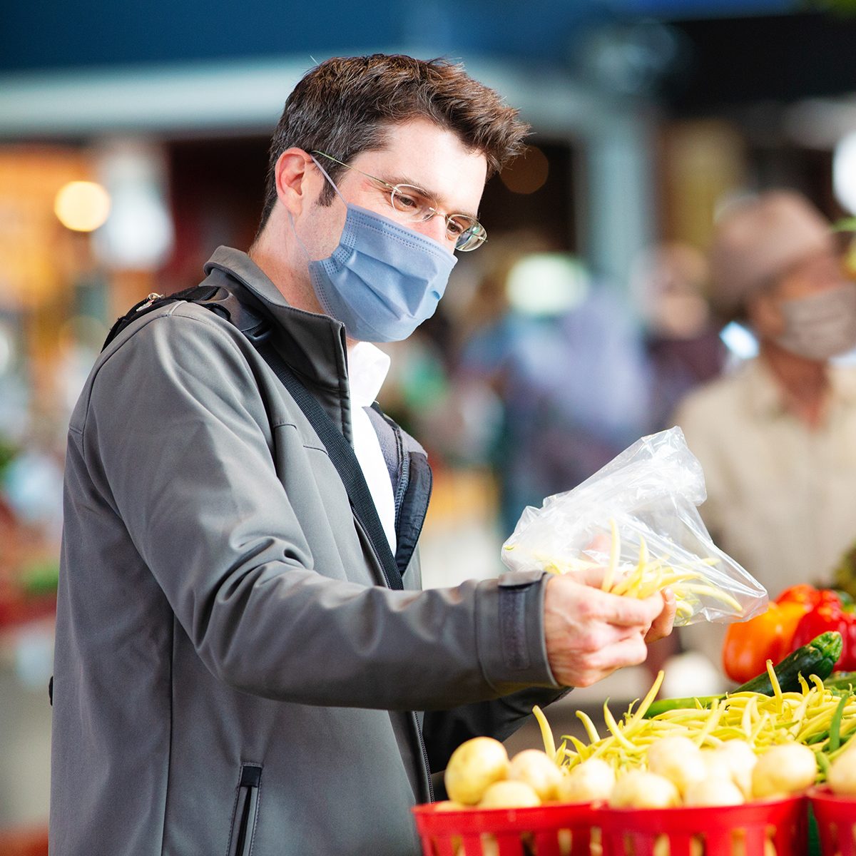 Young man wearing face cover selecting string beans at farmer