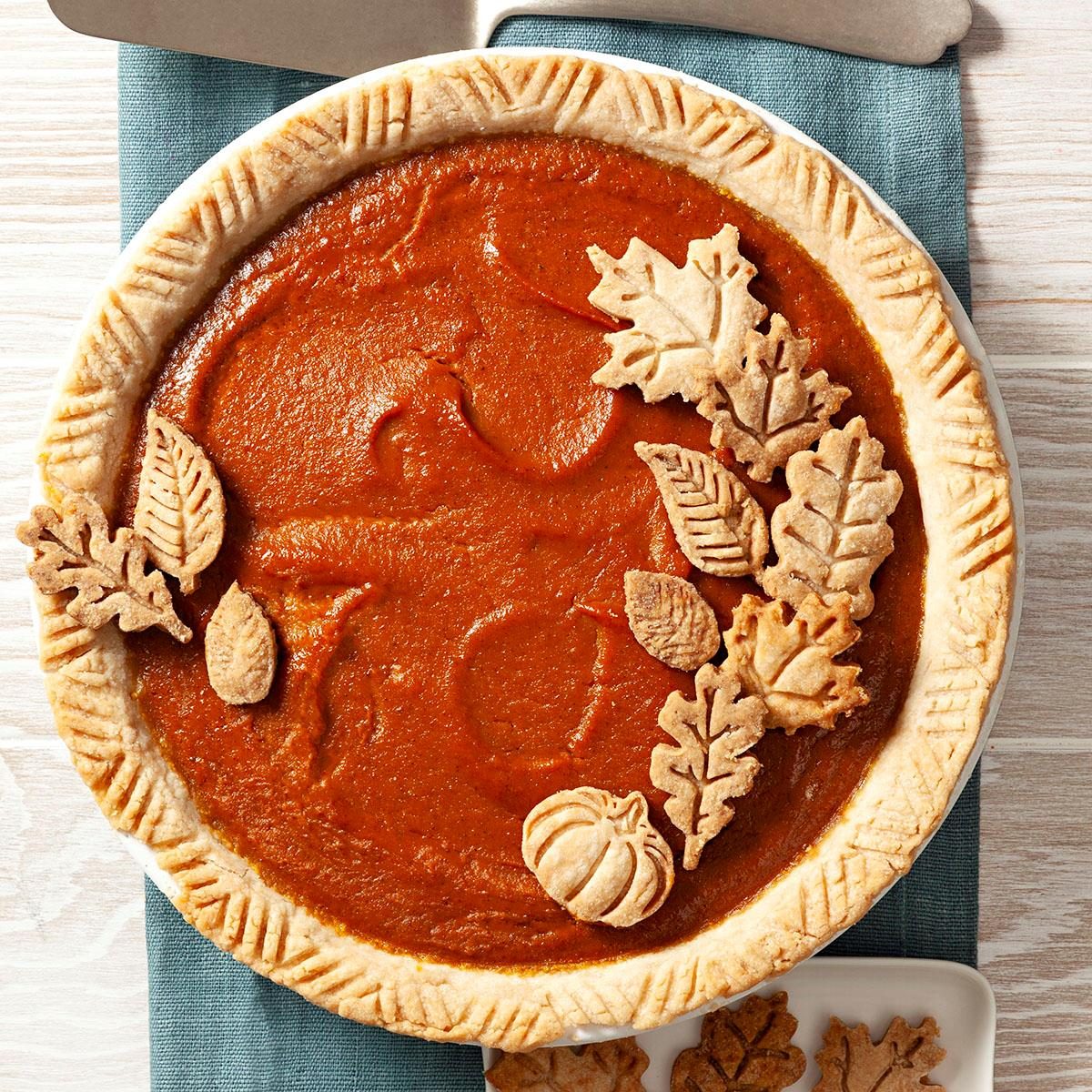 overhead shot; vertical shot; wooden background; Pumpkin Pie over green kitchen towel; garnishned with leaves cutout; pie server placed on kitchen towel