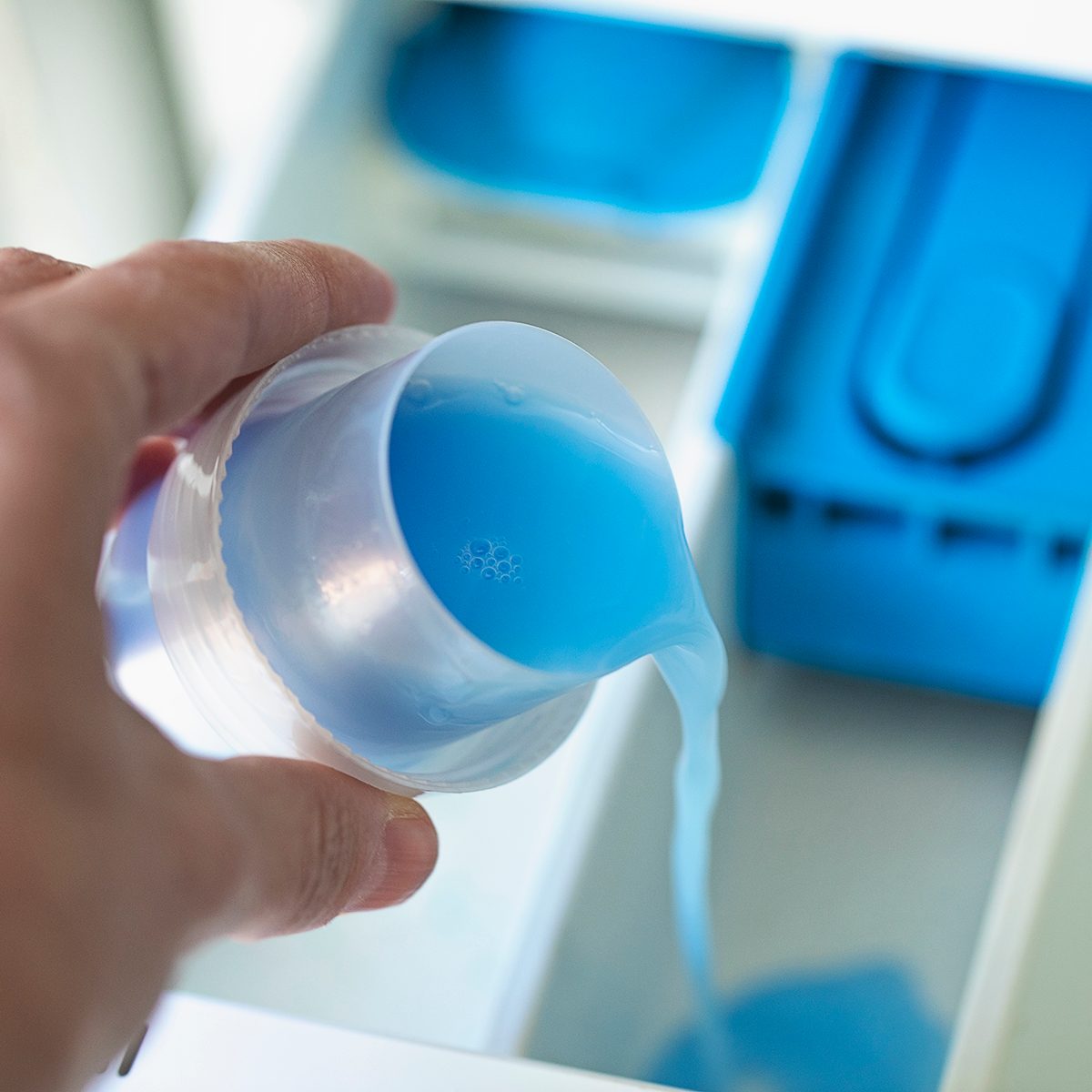 Close up of hand adding fabric softener to washing machine
