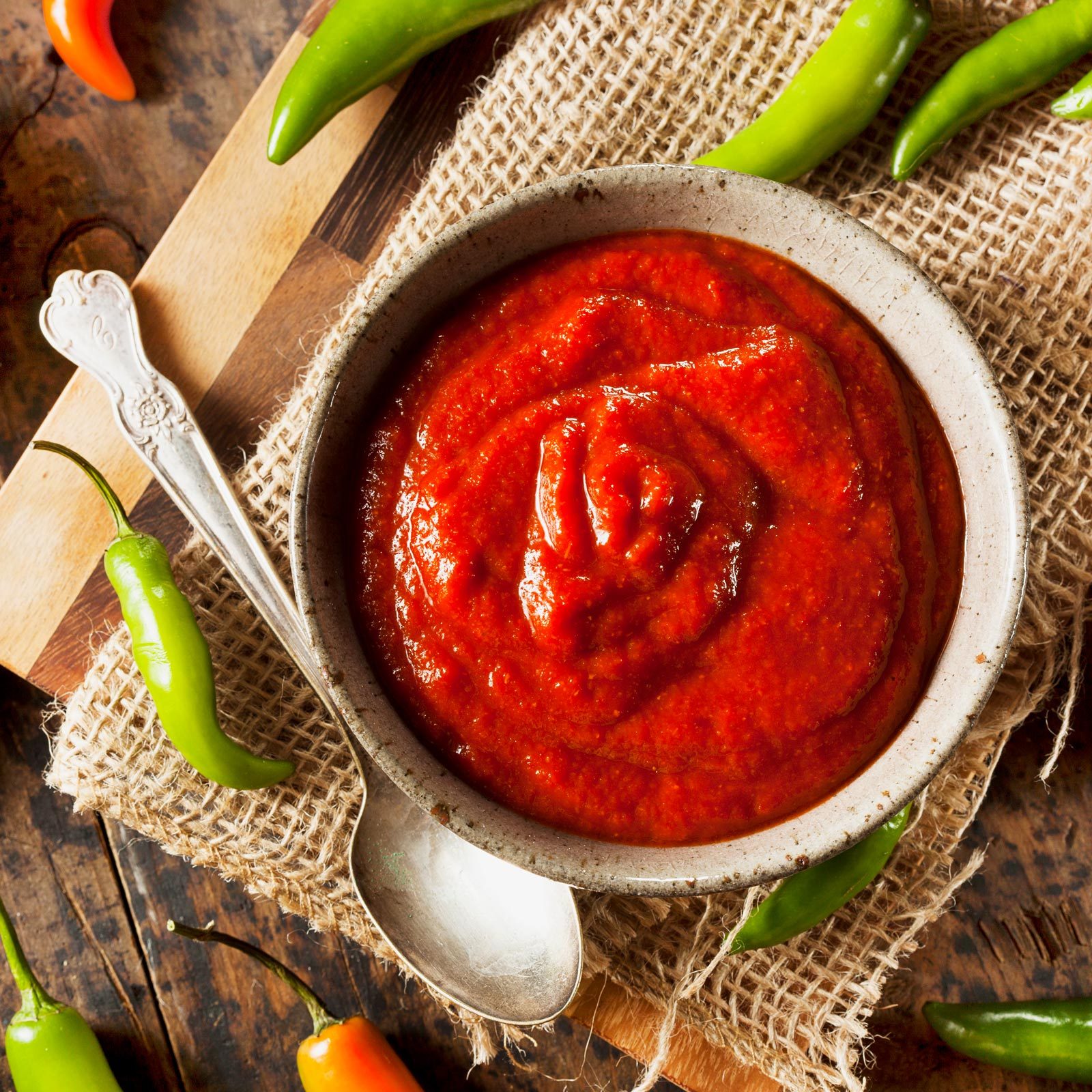 sriracha in a bowl with a spoon and peppers around it