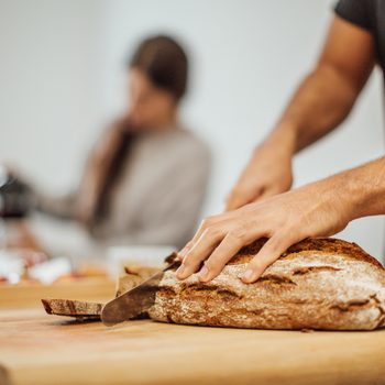Young man slicing bread on cutting board in kitchen