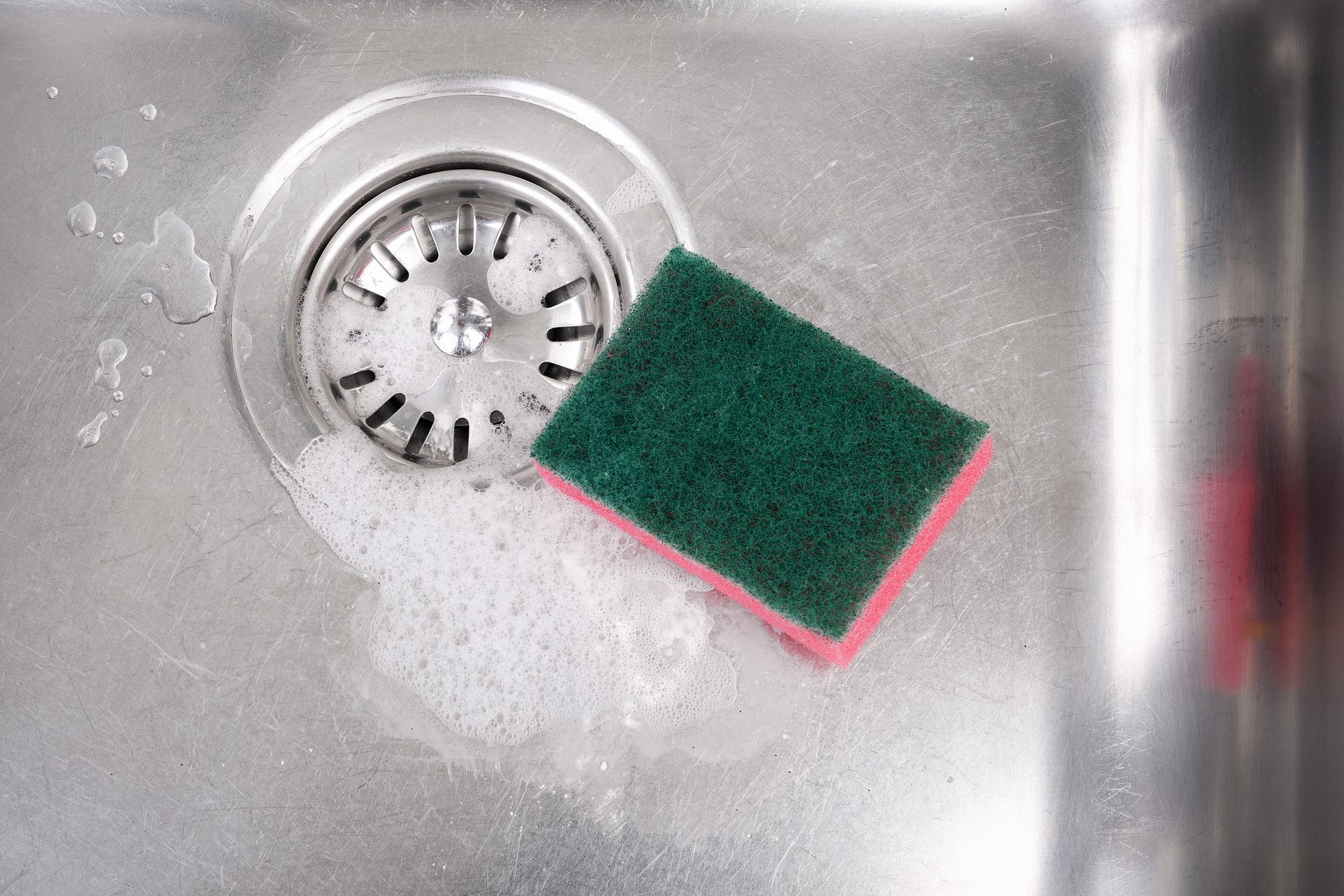 Stainless steel kitchen sink with soap suds and cleaning sponge