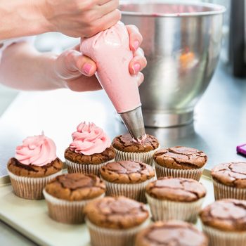 woman in bakery shows how to use a piping bag to decorate cupcakes