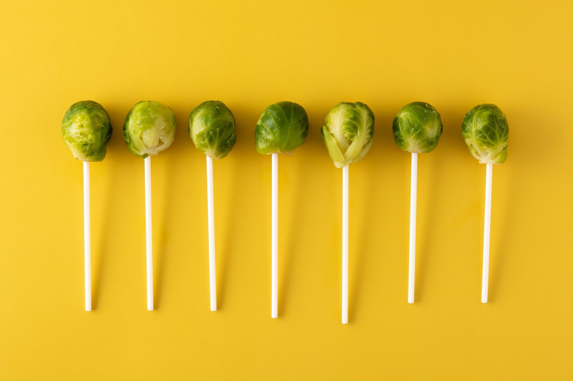 Set of brussel sprouts with lollipop sticks on yellow background