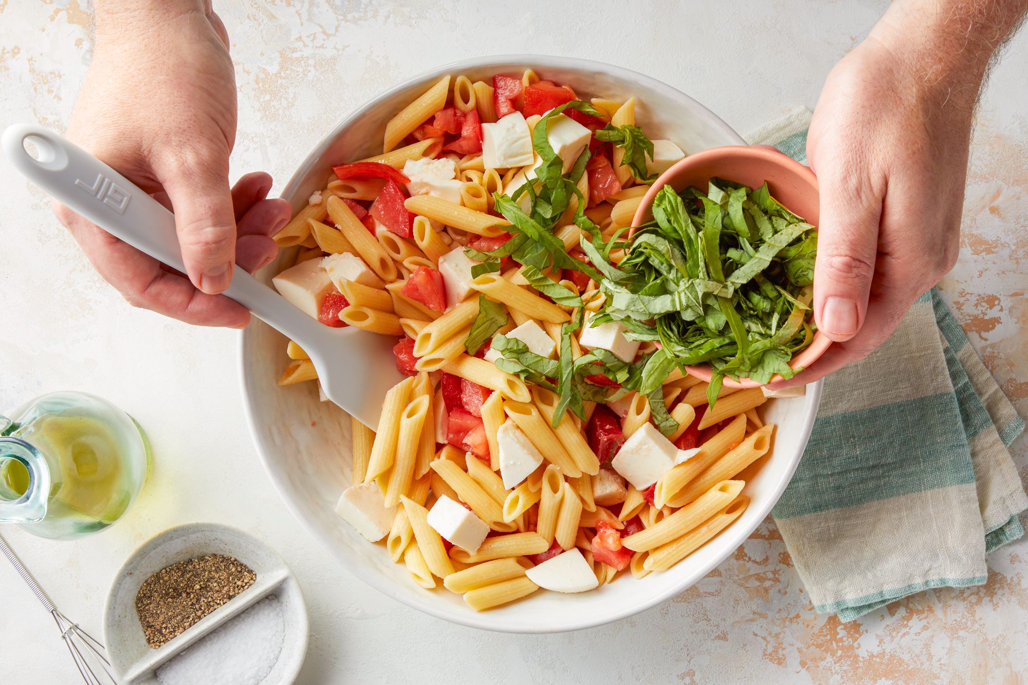 Mixing Pasta, Tomatoes, Mozzarella Cheese and Basil in a Large Ceramic Bowl to make Caprese Pasta Salad