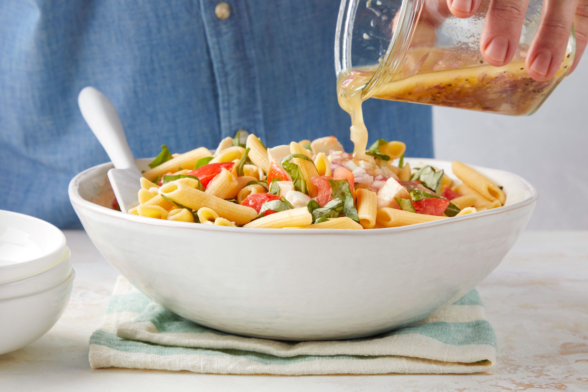 Pouring Mixed Liquid Ingredients on Caprese Pasta Salad in a Large Ceramic Bowl