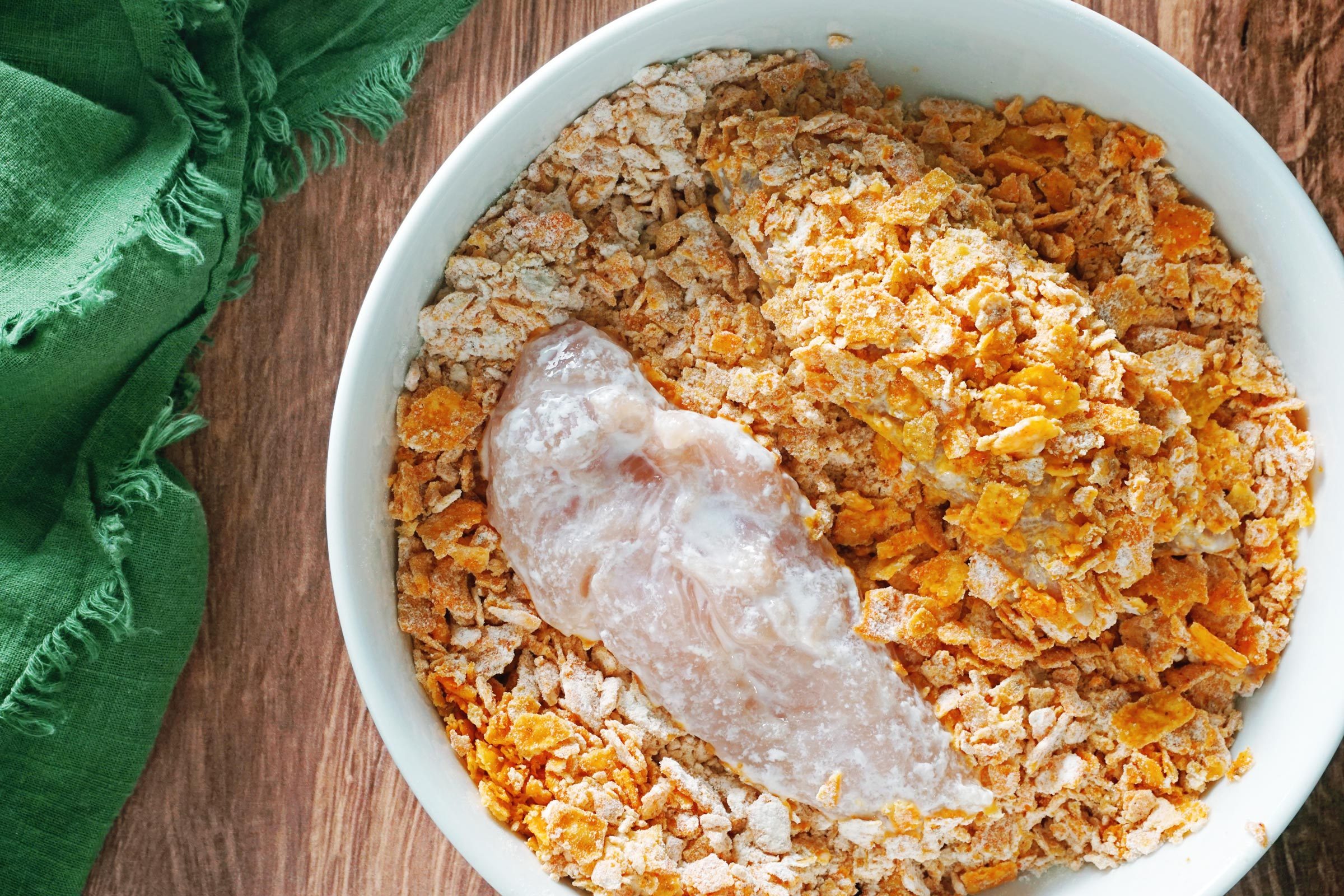 raw chicken getting covered in Dorito crumb mixture