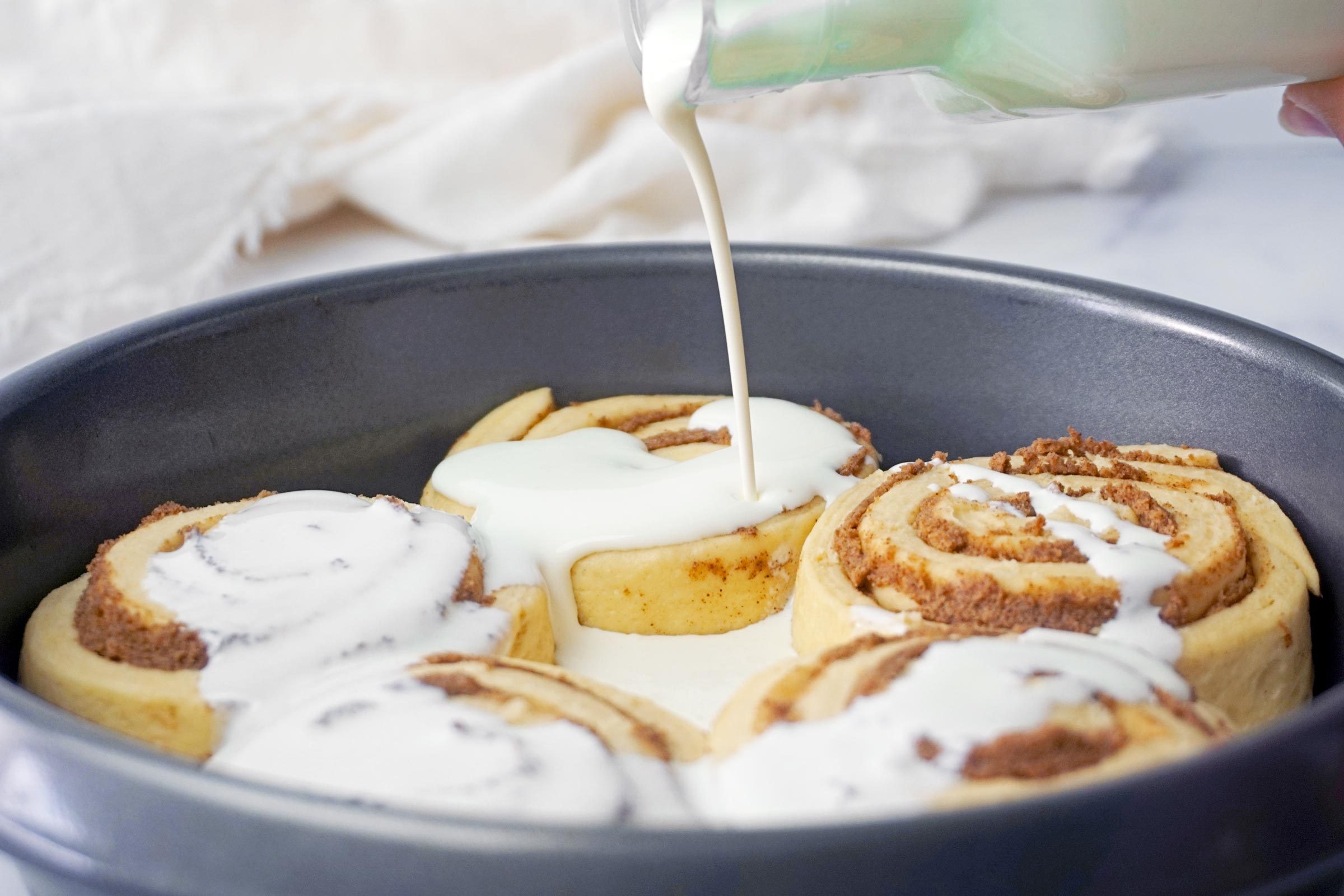 pouring cream on unbaked TikTok cinnamon rolls In a pan