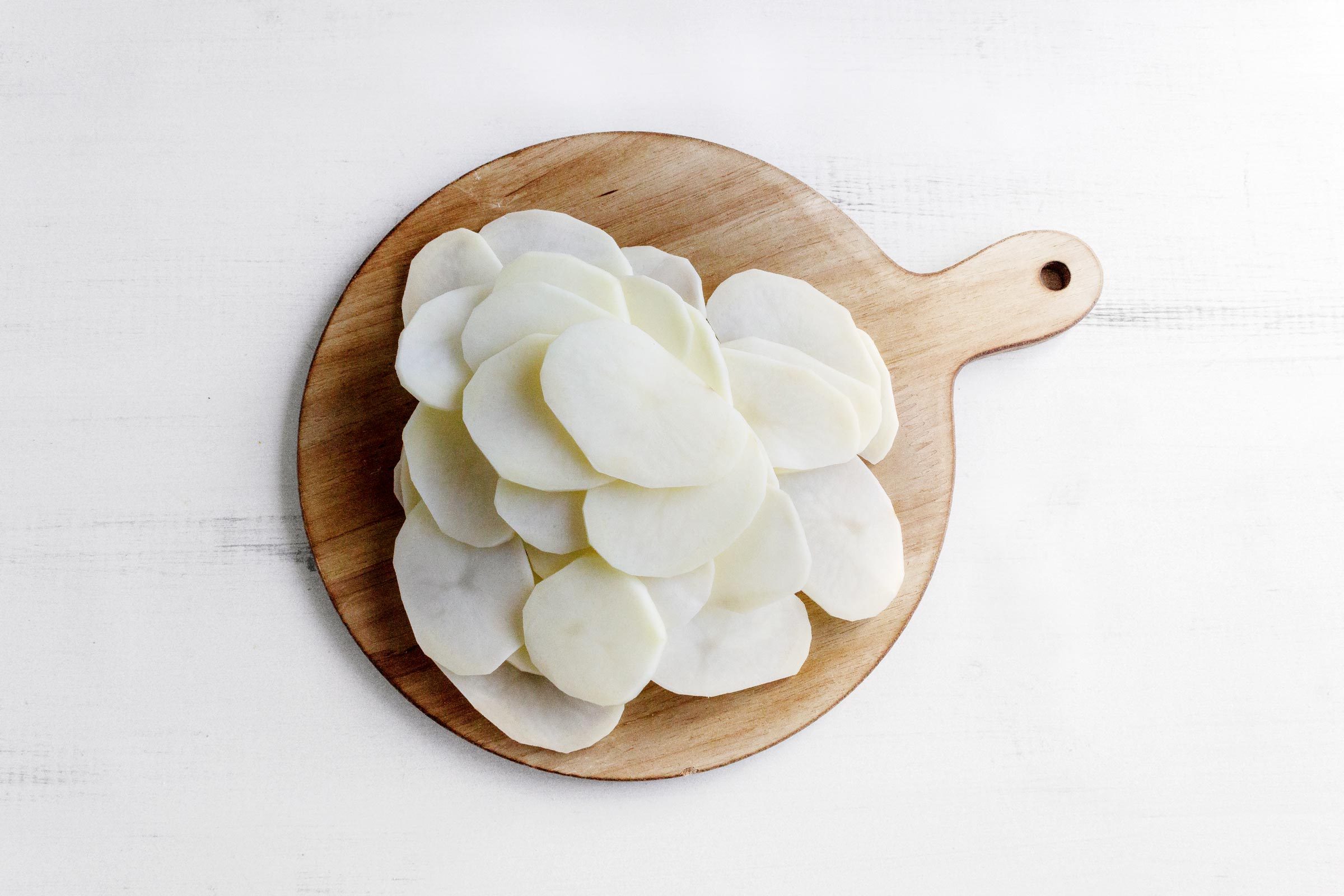 raw potato slices on a wood cutting board