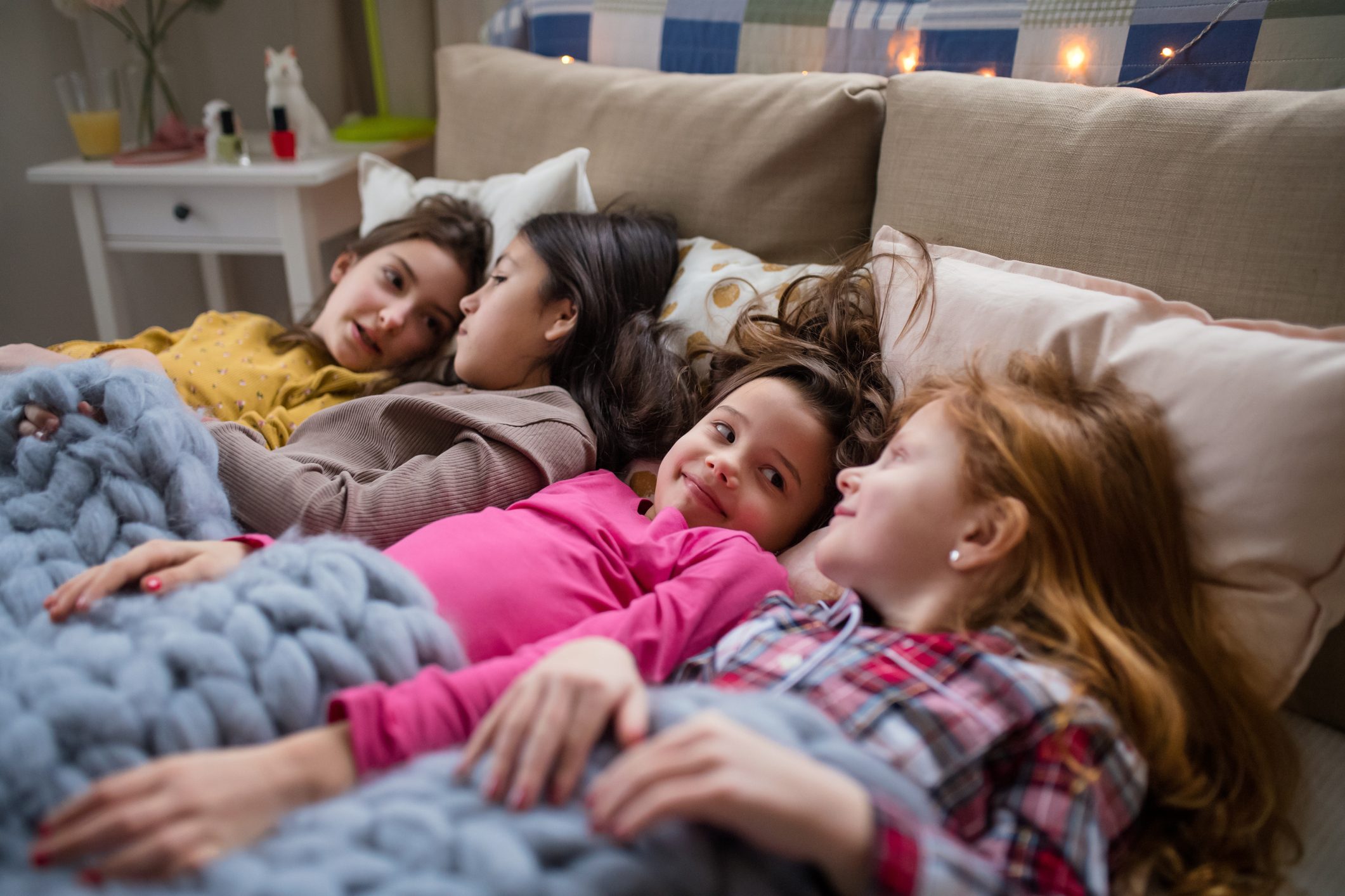 Group of small girl friends lying in bed, talking.
