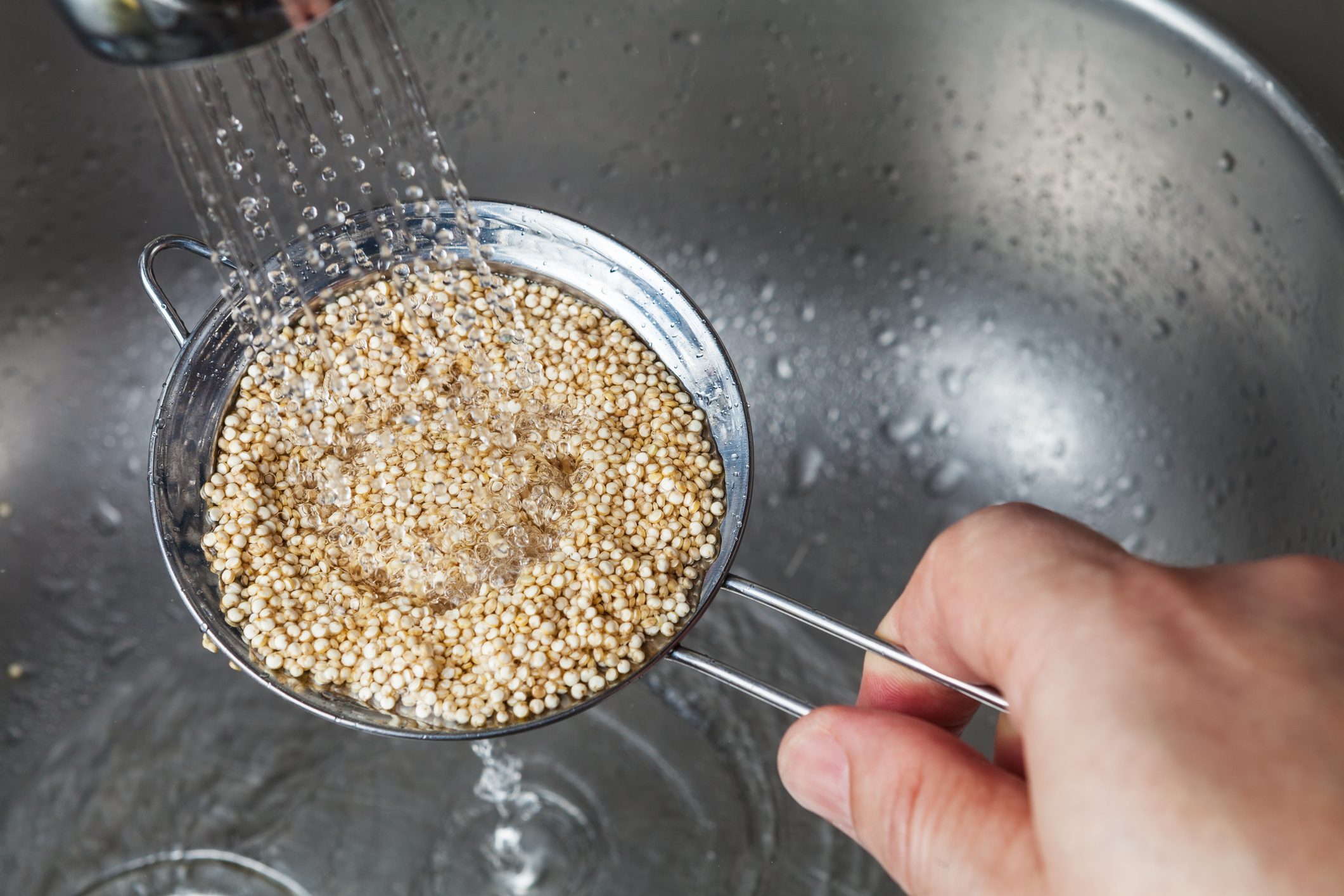 Man holding small strainer with raw quinoa seeds
