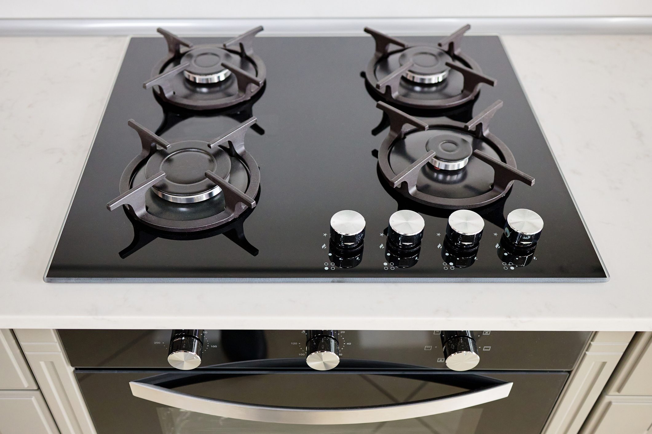 Modern built-in oven and gas stove classic design in dark tones under light stone marble or granite countertop in interior of contemporary kitchen.