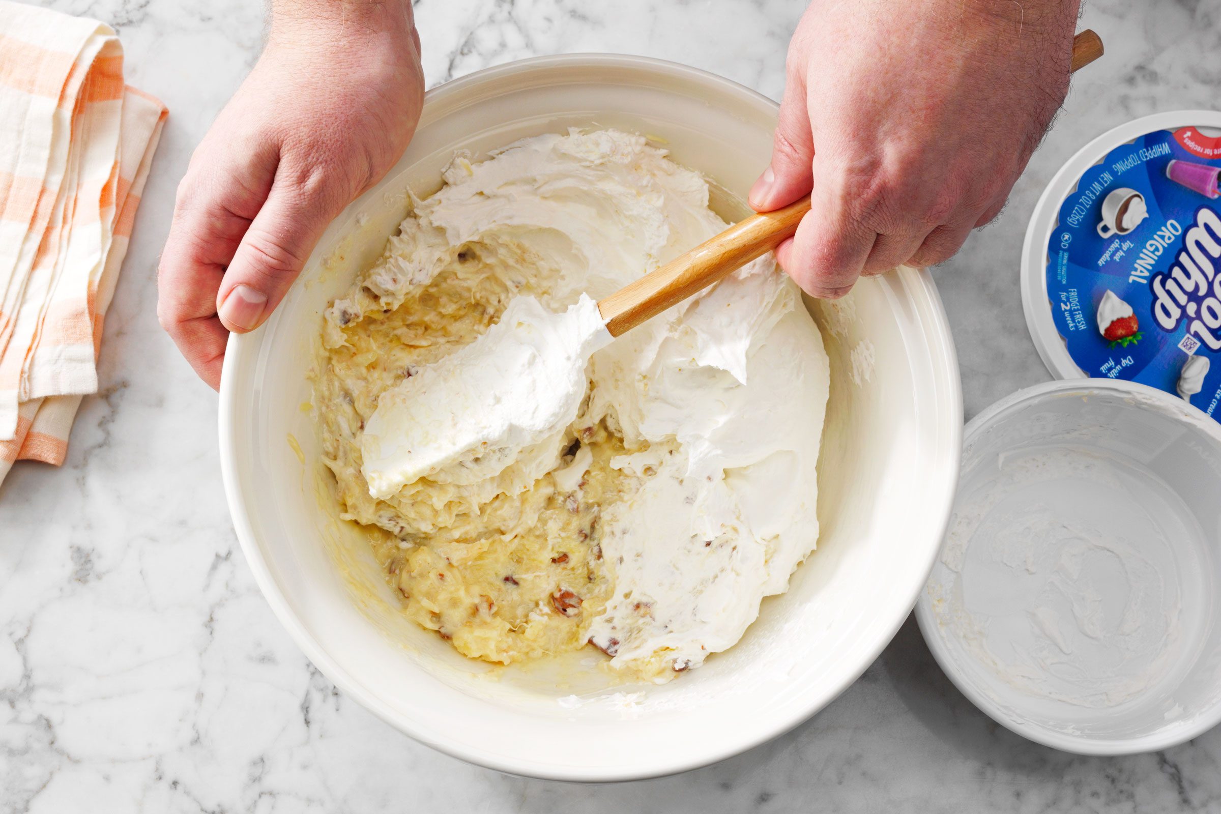 top view of a hand mixing pie filling with a rubber spatula in a large white mixing bowl 