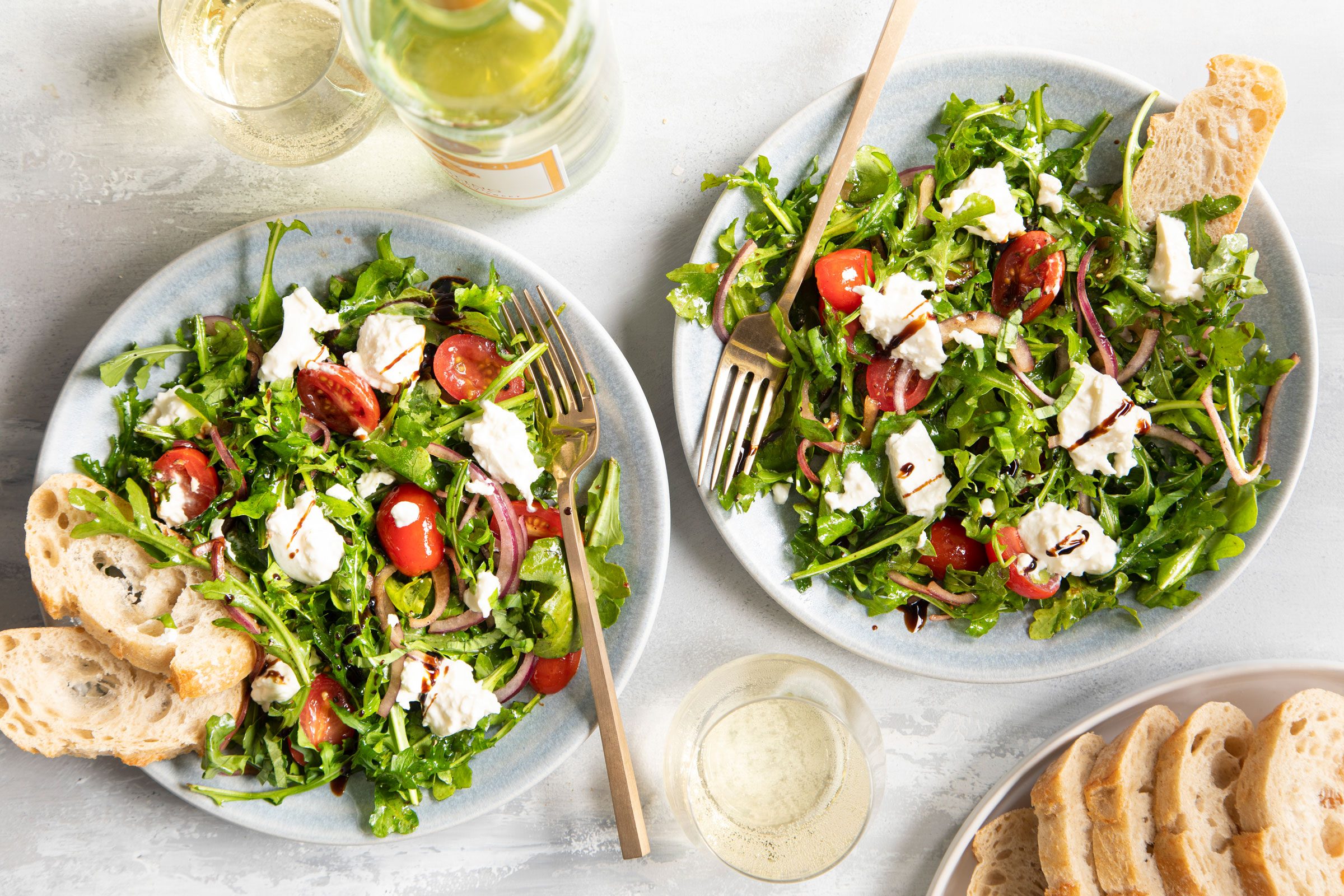 two plates with arugula topped with tomatoes, burrata cheese and balsamic