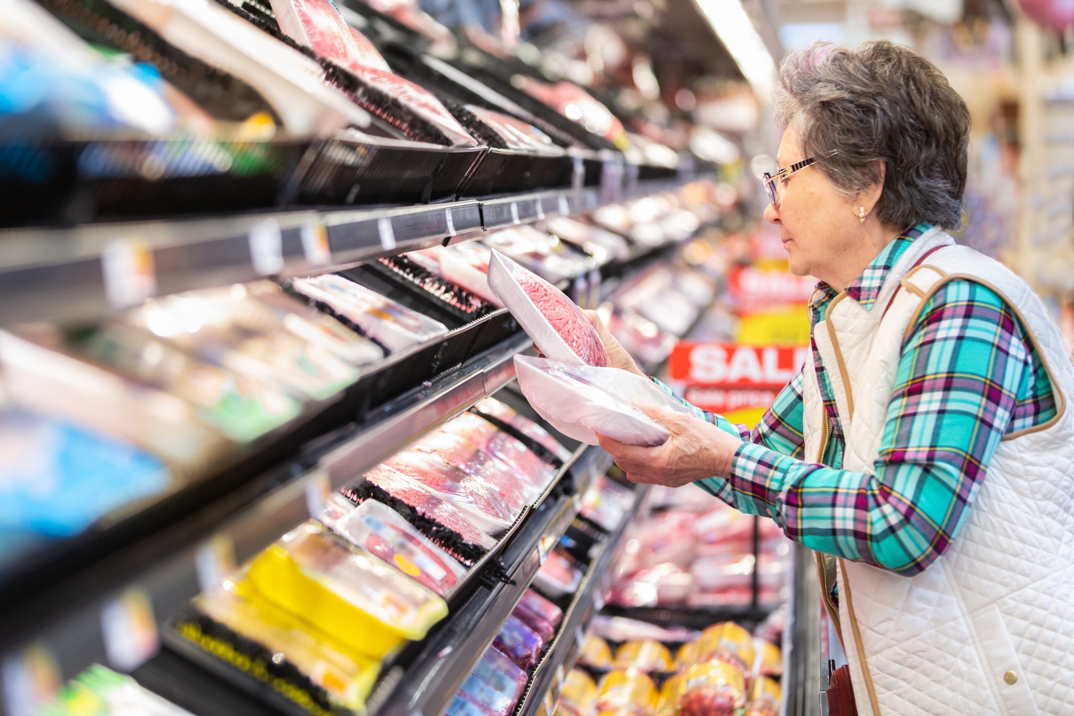 Senior woman selecting ground beef in the meat department.