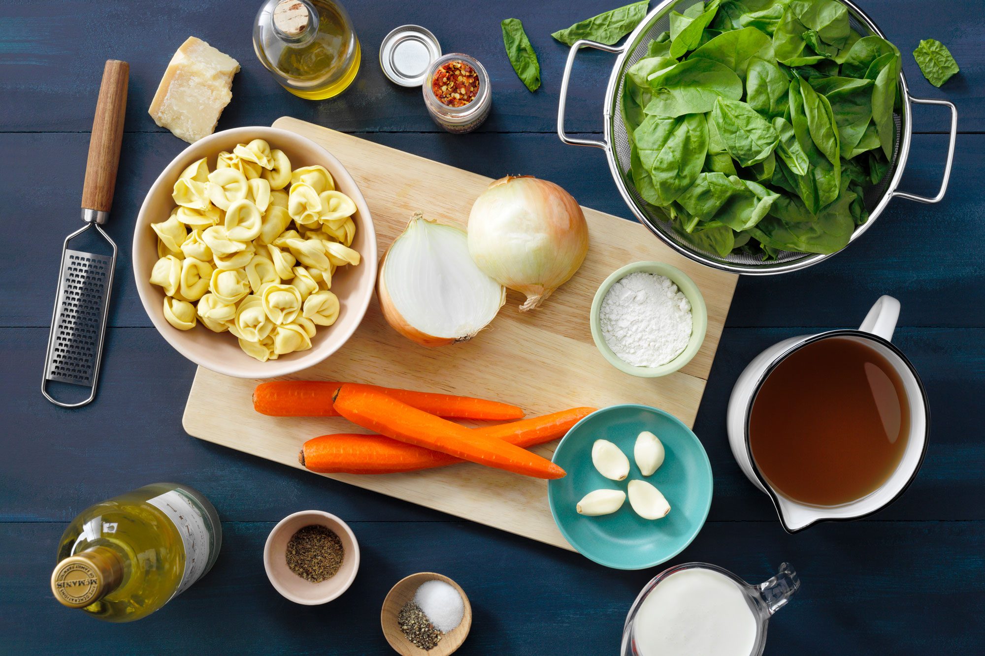 creamy tortellini soup ingredients laid out on navy wood surface