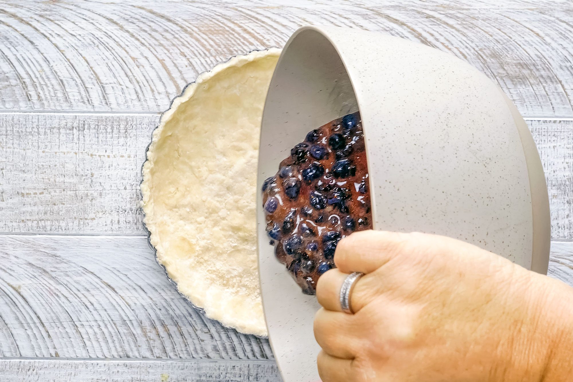 Pouring Blueberry Tart Filling on pressed dough in tart pan on wooden surface
