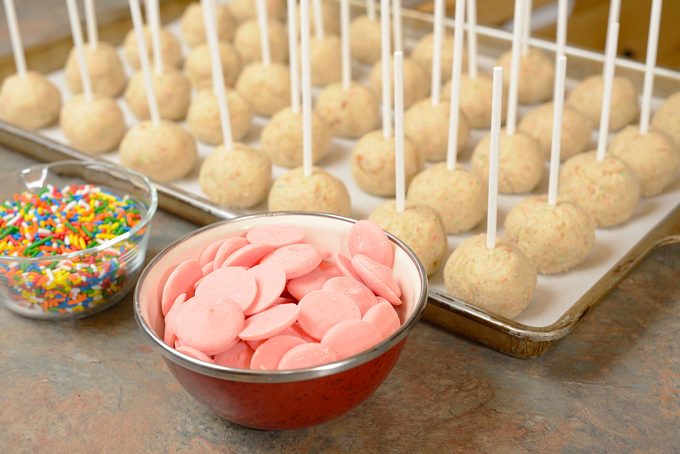 Undipped cake pops with sticks inserted near bowl of pink candy melts and colorful sprinkles