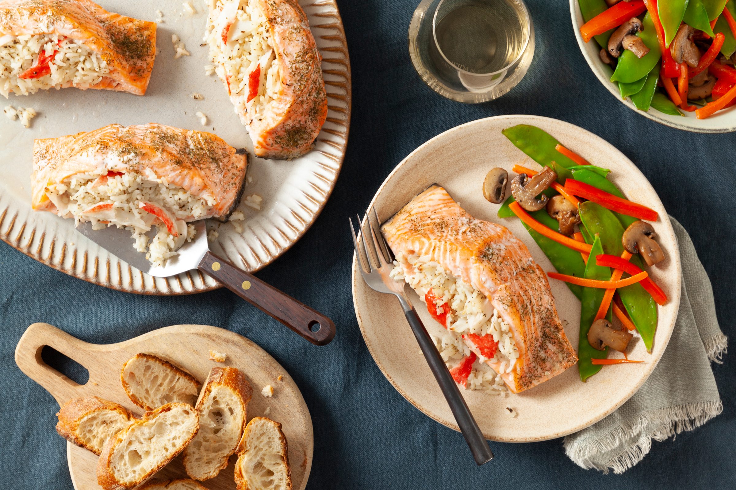 stuffed salmon on a plate with a side of mixed veggies and a serving platter with more stuffed salmon off to the side