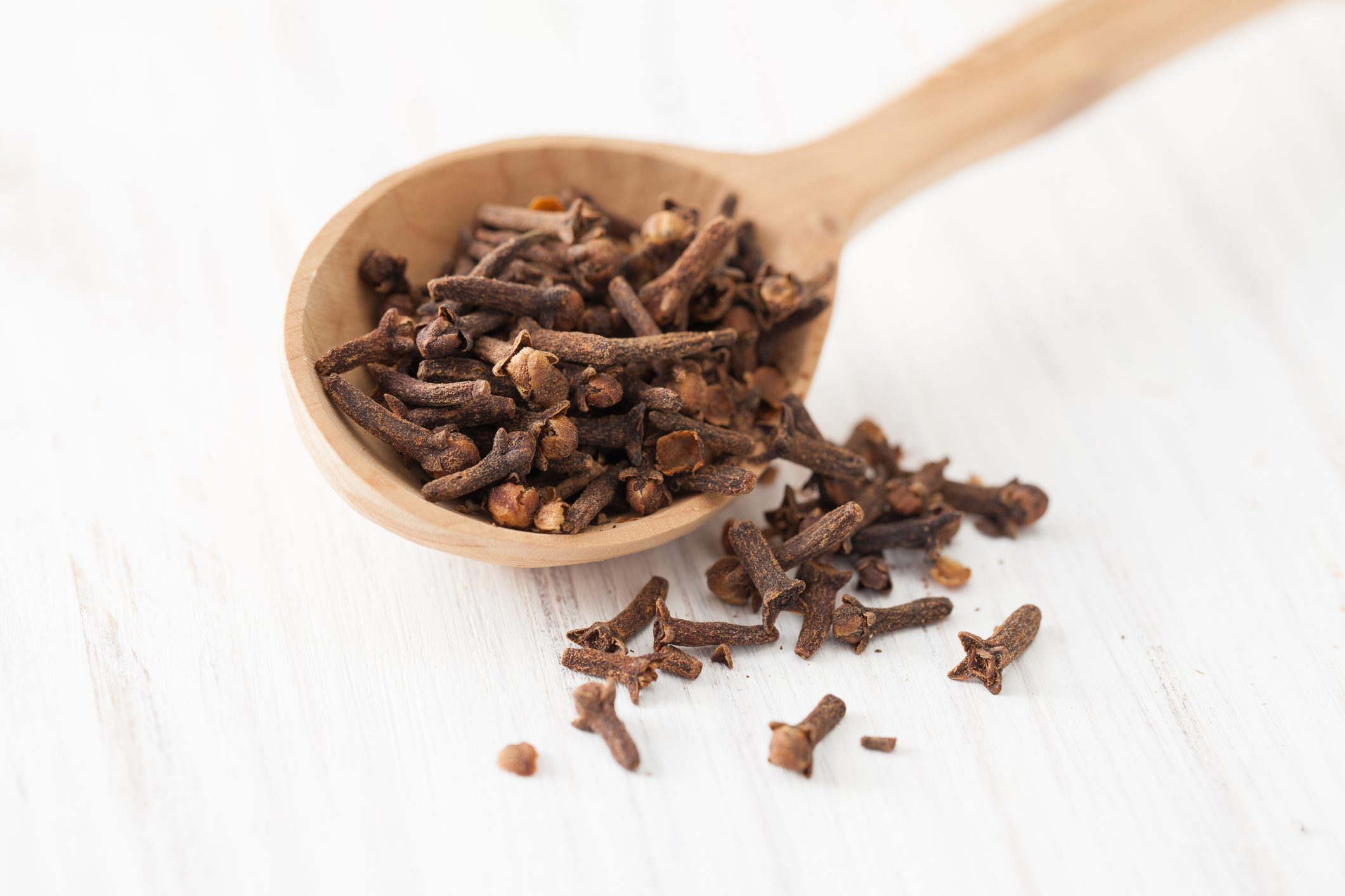 Cloves in wooden spoon on white wooden table