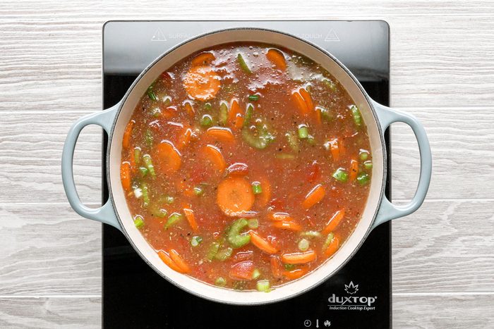 Lentils, tomatoes, carrots and other vegetables mixed inside a large dutch oven