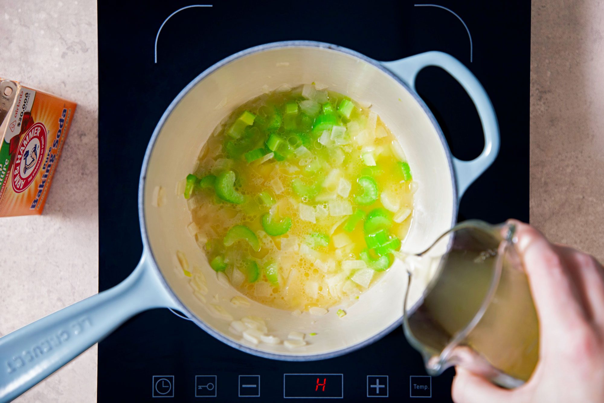 A Person Pouring Broth Into A Saucepan on Induction Cooktop on A Marble Kitchen Top