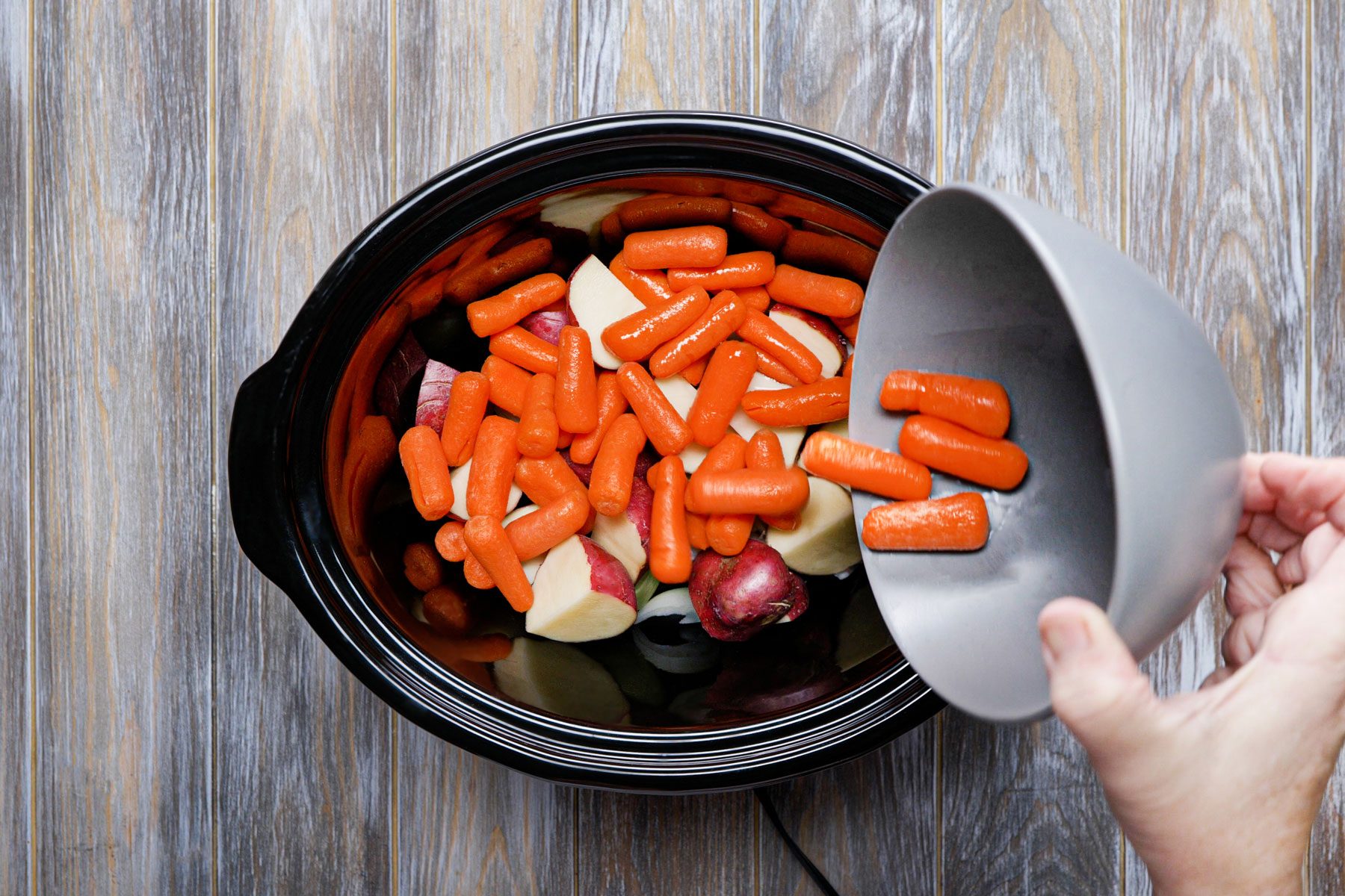 Placing onion, potatoes and carrots in a slow cooker 