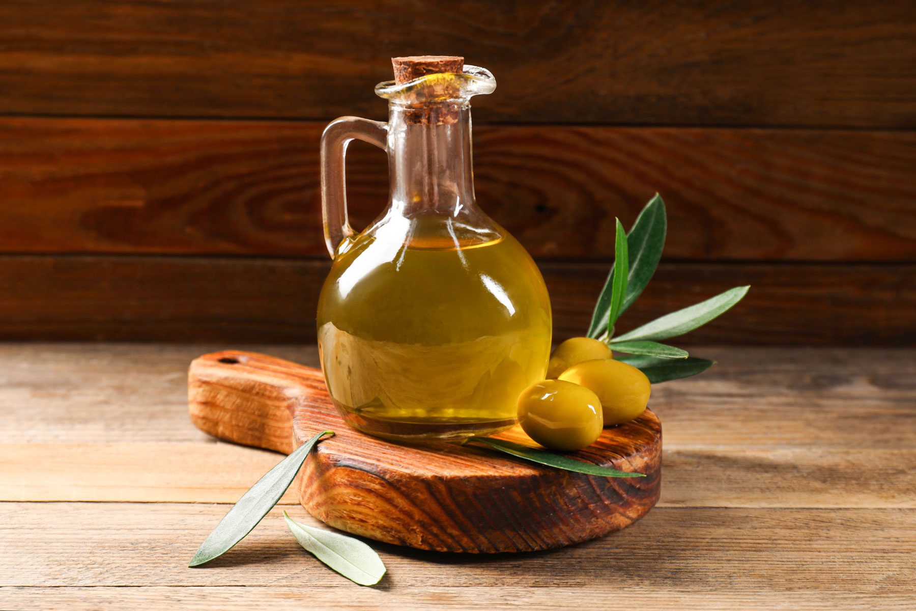 Jug olive oil, and green leaves on wooden table