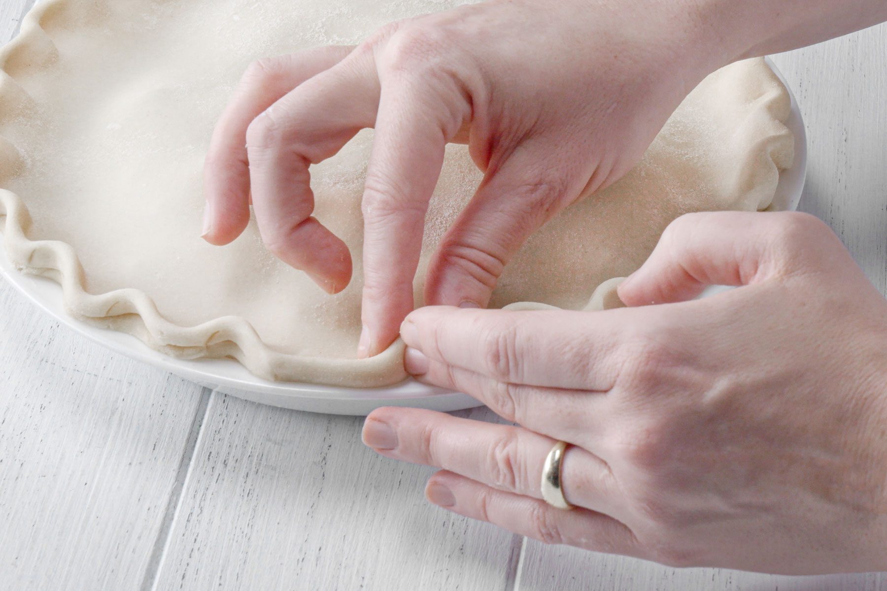 A person sealing the edges of the pie crust 