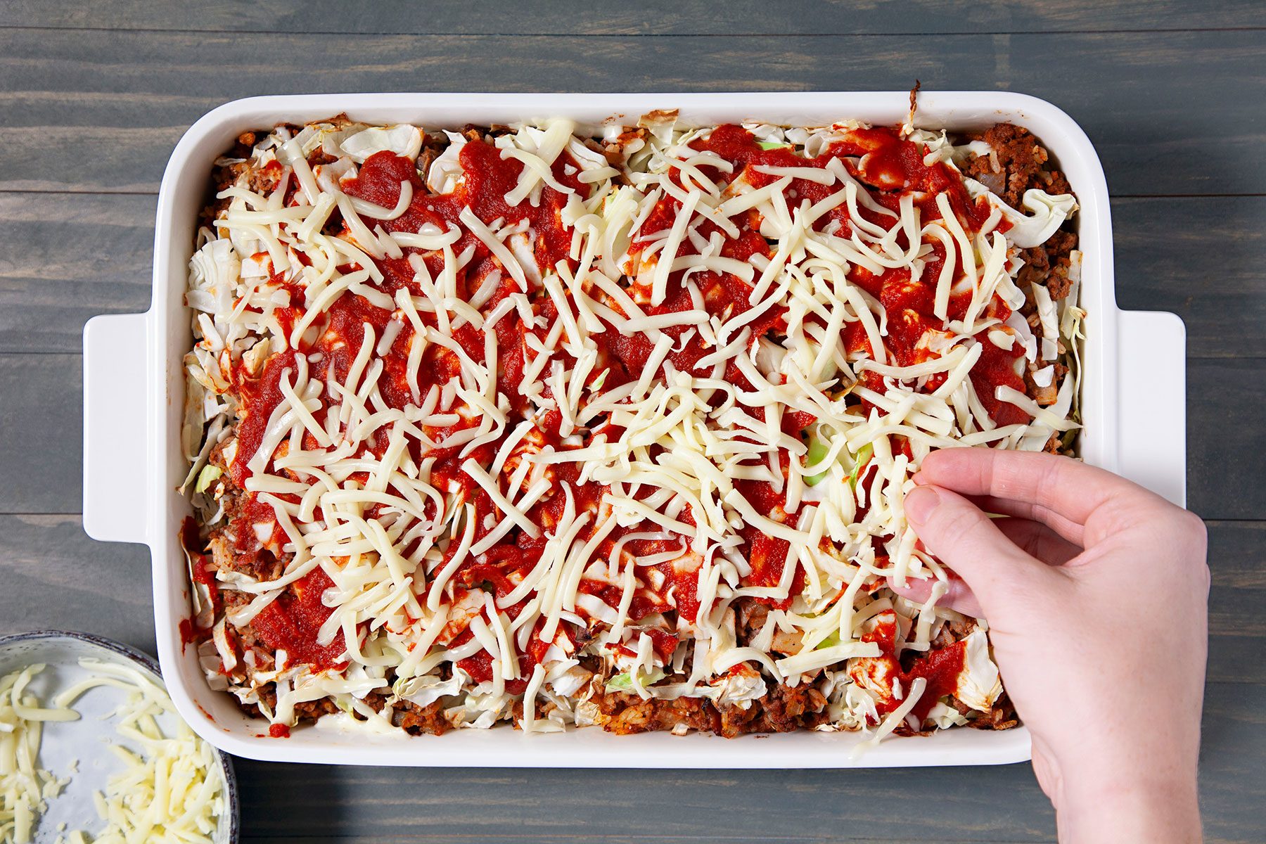 Sprinkling cheese on beef mixture in casserole