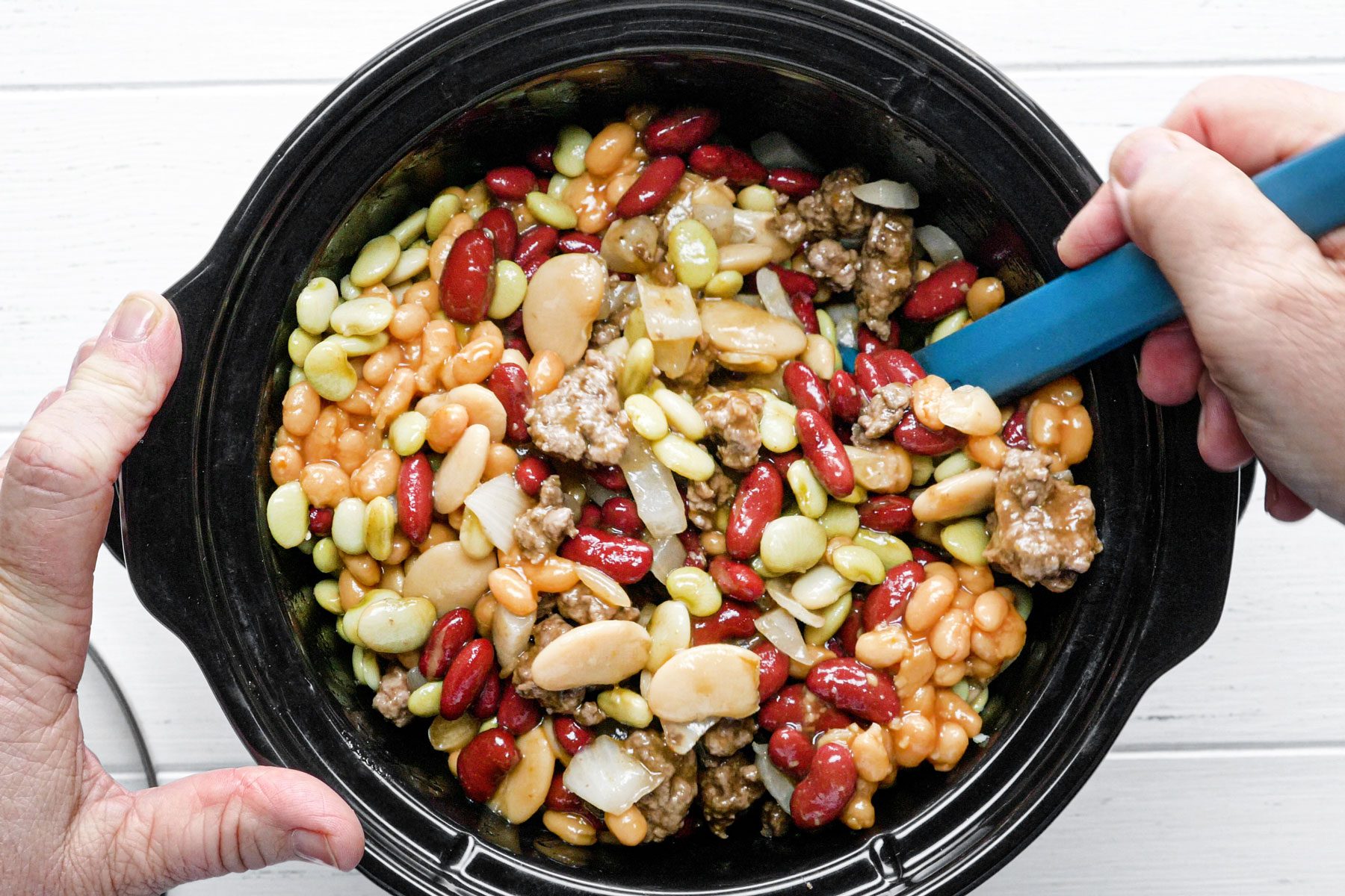 Mixing the beans with beef in a slow cooker on a wooden table