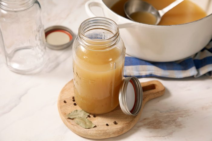 A jar of chicken broth on a cutting board next to a white pot