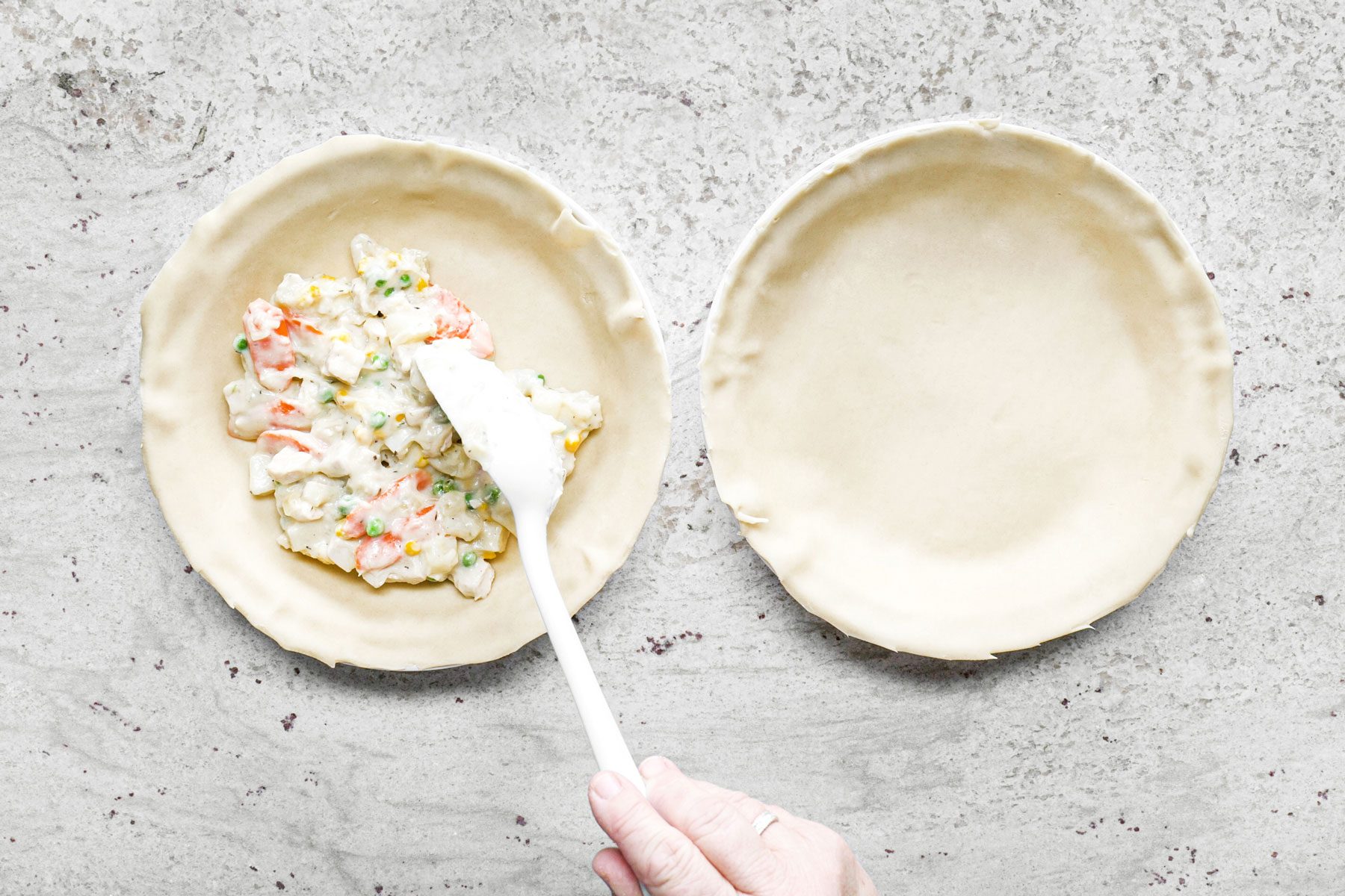 Adding the filling to pie plate with a spoon on a marble surface.