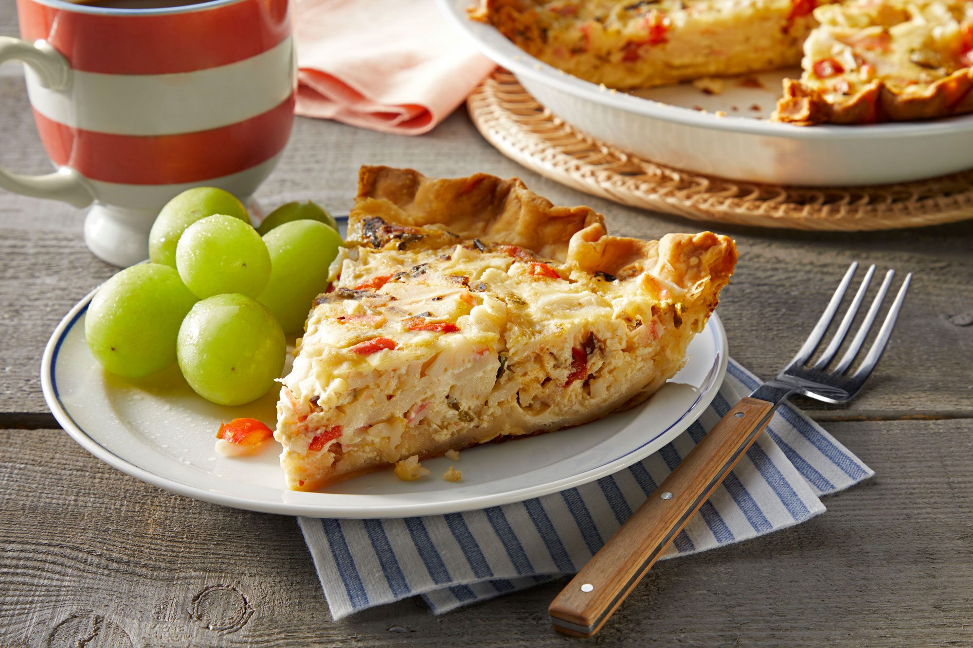A Piece of Crab Quiche Served on White Ceramic Plate with Fork on Wooden Surface