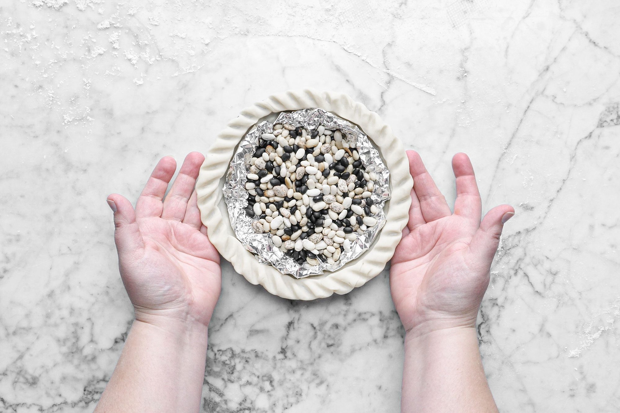 a person's hands holding pie crust with dried beans in foil paper on it