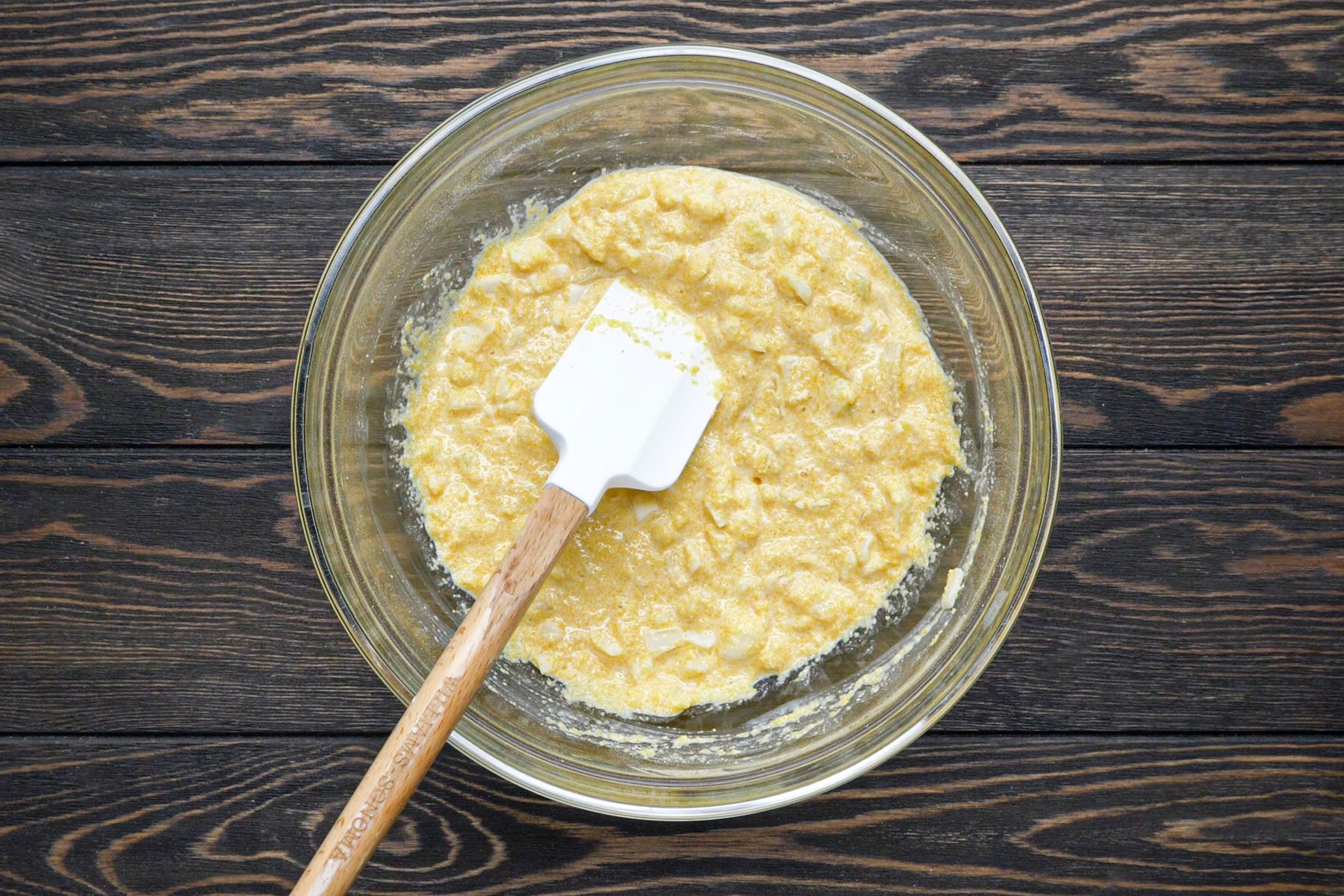 Egg, milk and onion mixed in a large bowl with a spatula
