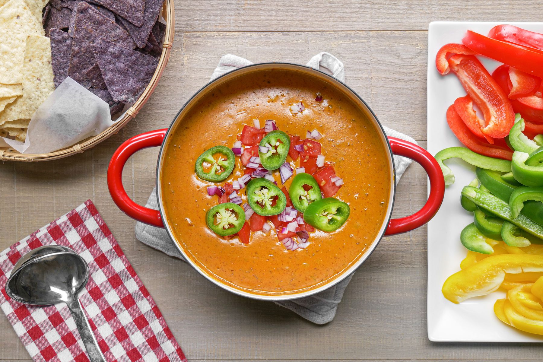 Chili Cheese Dip served in a pan with tortilla chips, pretzels and peppers on the side