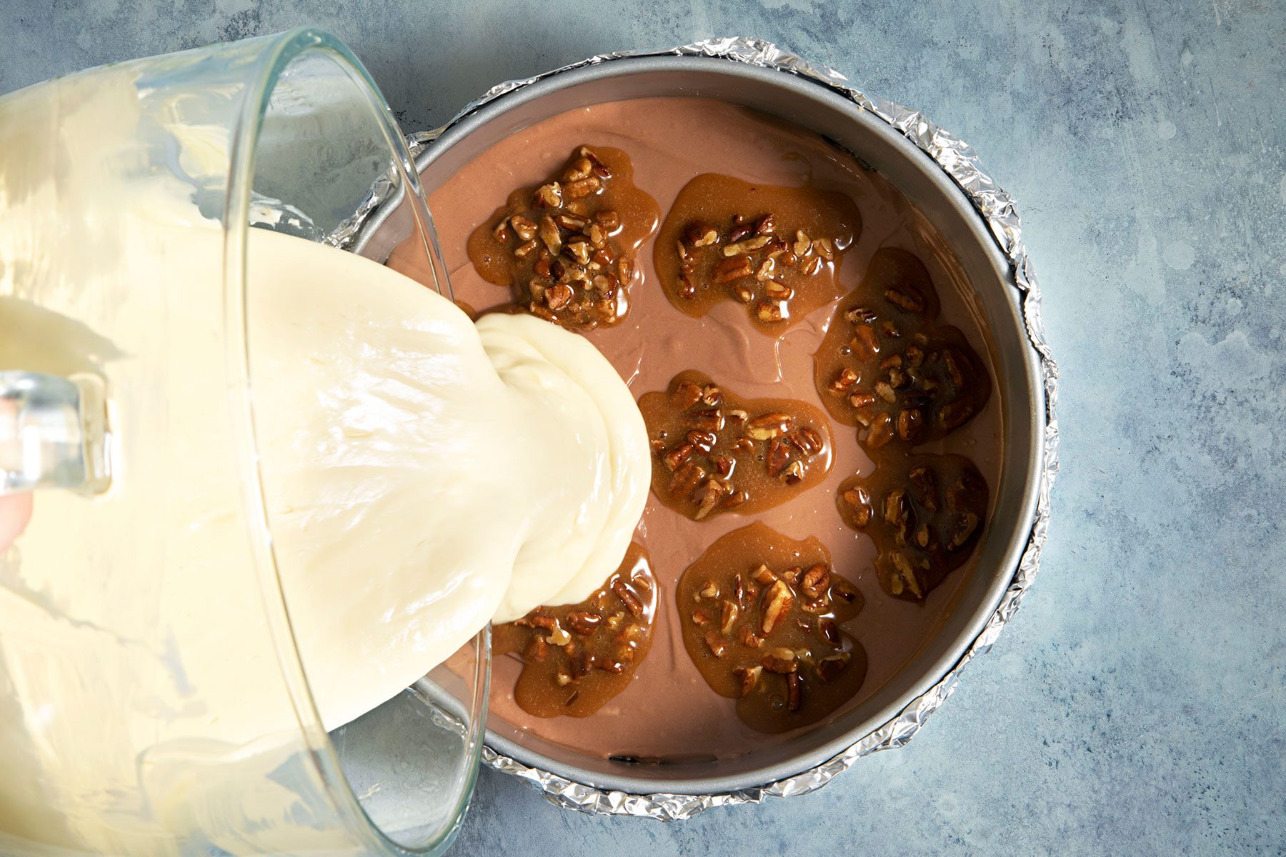 Adding remaining batter over pecans mixed with caramel toppings
