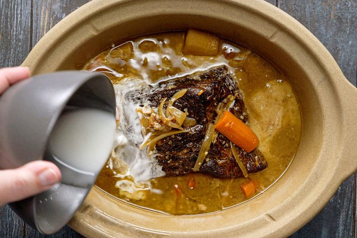 Pouring Cornstarch Mixture into a Slow Cooker Full of Rump Roast