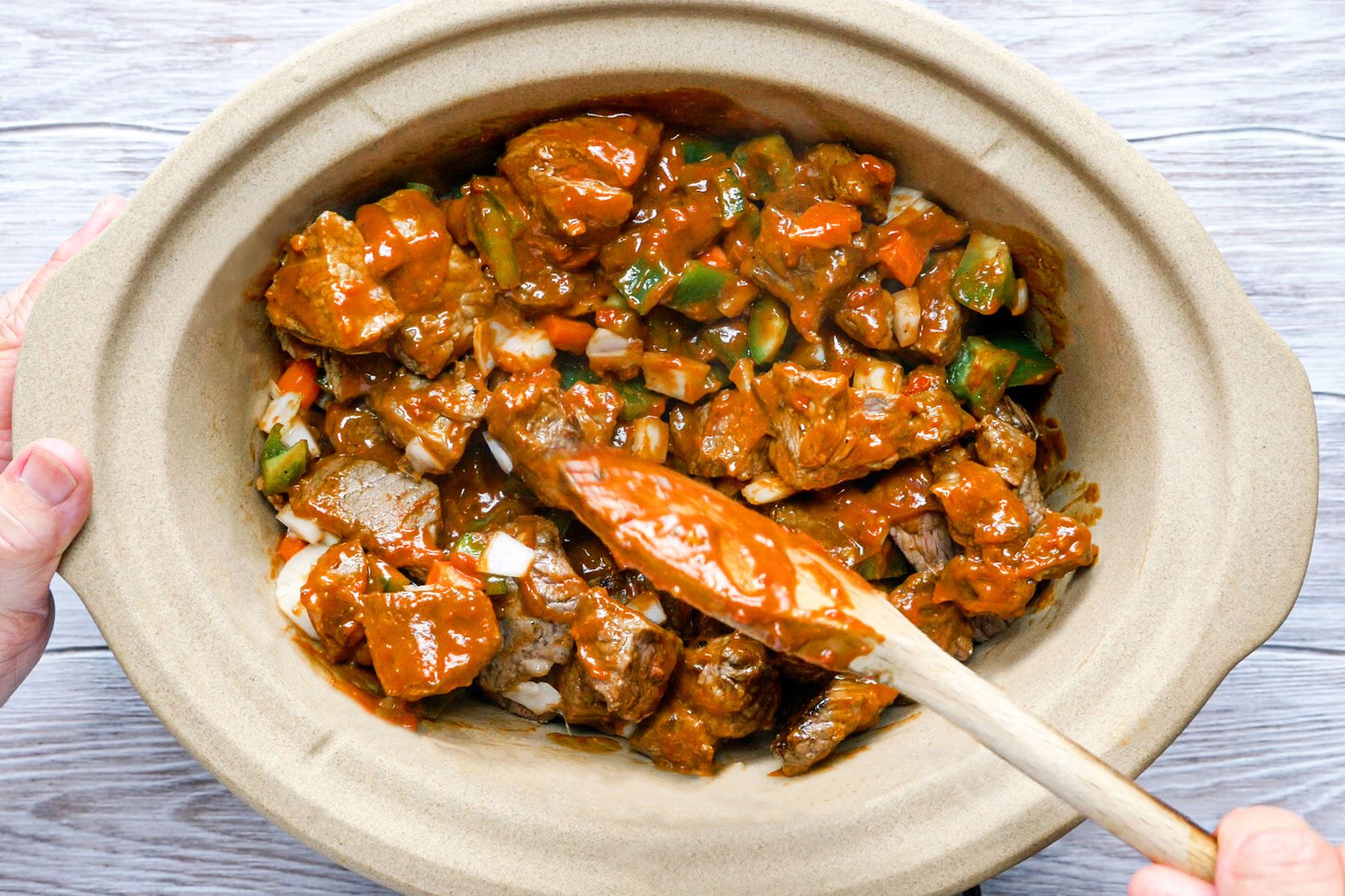 Mixing the meat with sauce in slow cooker using a spatula