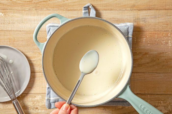 A hand with a spoon of pudding over the saucepan