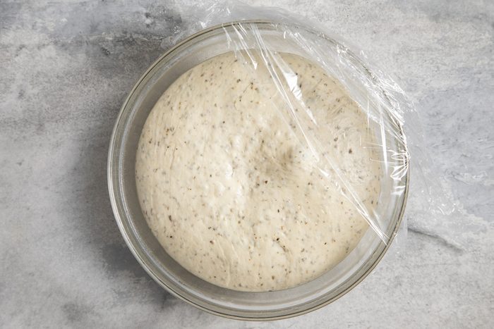 A bowl of pizza dough in plastic wrap