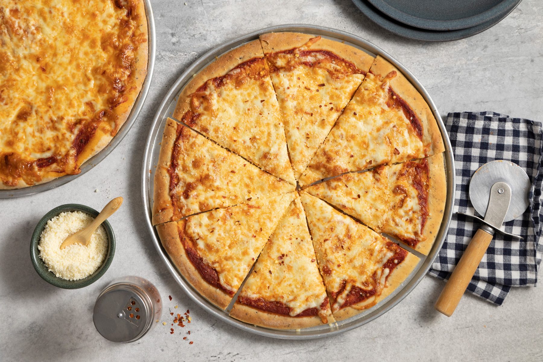 A cheese pizza pan with Parmesan cheese & crushed red pepper flakes