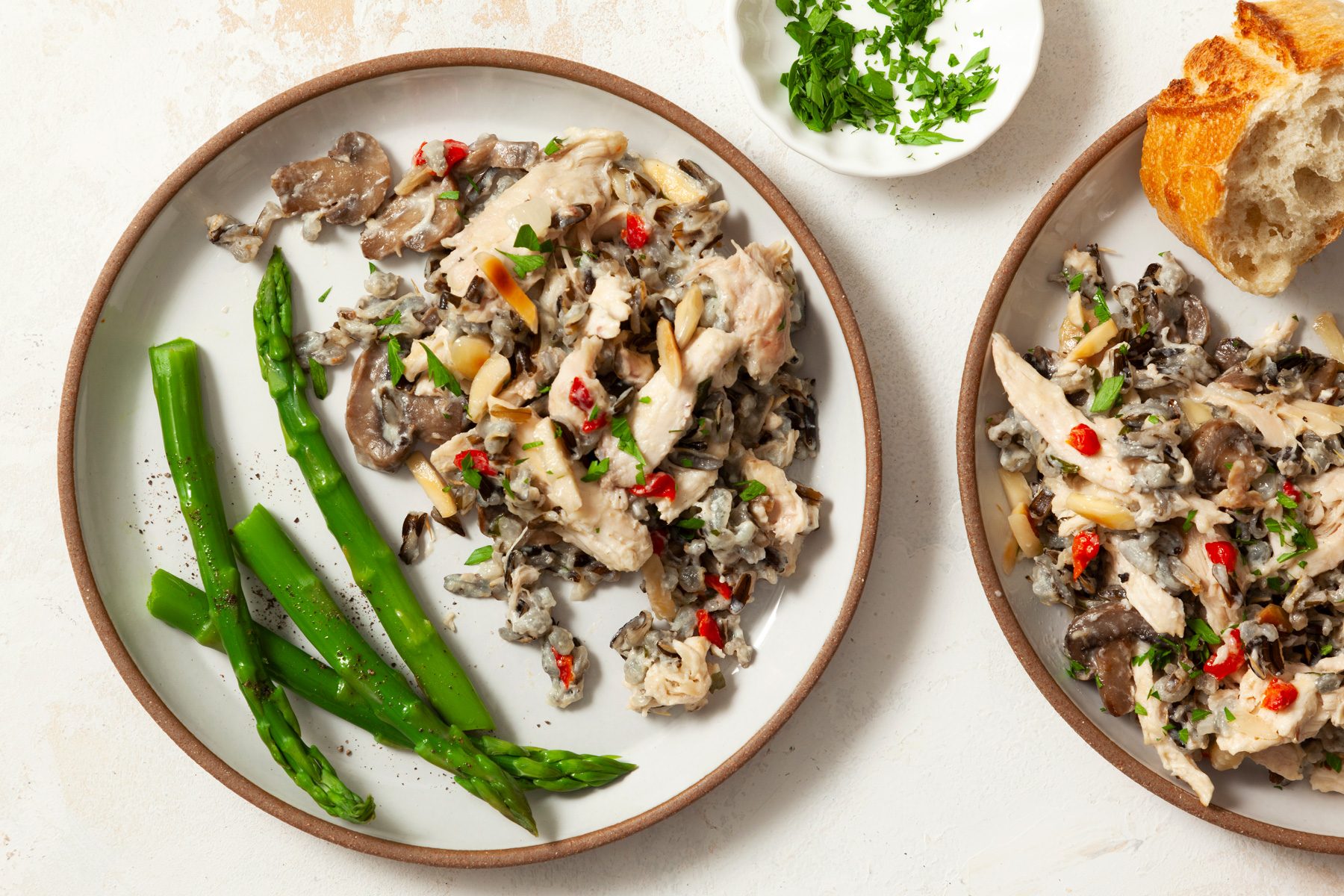 Two plates of chicken wild rice casserole with bread and asparagus